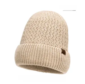 Detail of beige knit beanie showing thick wool texture and brown leather snowflake tag