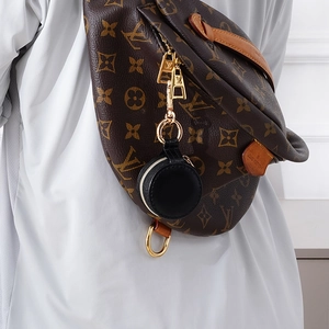 Black leather mini round jewelry pouch hanging on a bag with gold zipper detail