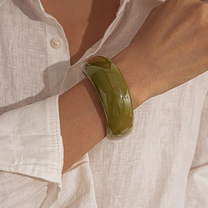 Close-up of olive green acrylic wide bangle worn on wrist with white linen shirt