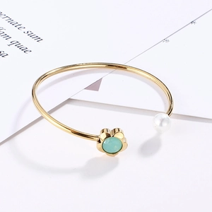 Detail of gold open bracelet featuring a green crystal flower and white pearl
