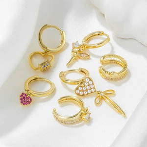 Golden earring set featuring bow and heart charms with pearls on white silk