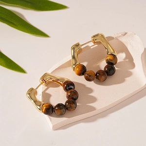Boucles d'oreilles créoles dorées en C avec perles œil de tigre marron sur socle en pierre