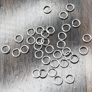 Silver metal open jump rings for DIY jewelry making on a dark wood background