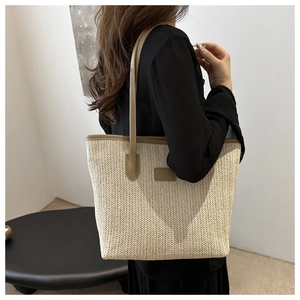 Detail of woven tote bag with cream herringbone texture and light brown leather handle