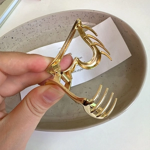 Detail of hollow gold heart hair claw clip being opened by hand to show metal spring