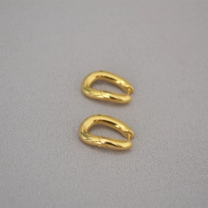 Detalle macro de pendientes en forma de U de latón bañado en oro con acabado pulido