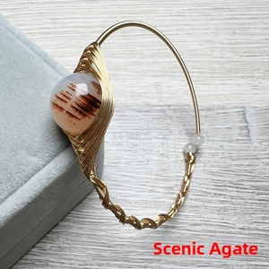 Macro detail of handmade gold wire-wrapped bracelet featuring a scenic landscape agate