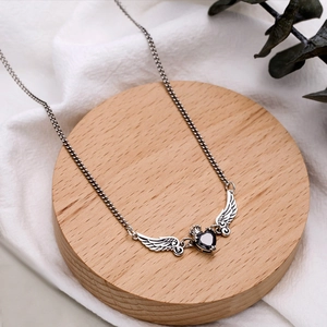 Detail of silver crown wings necklace with black heart pendant on a rustic wooden tray