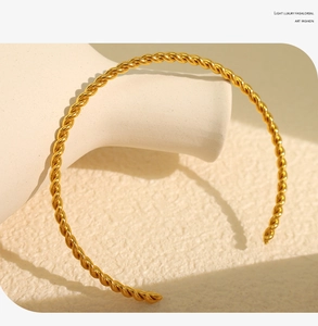 Detail shot of a polished gold twisted cable open cuff bracelet on a white texture background
