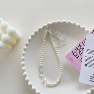 Beaded phone charm with white faux pearls and transparent butterfly pendant on a tray