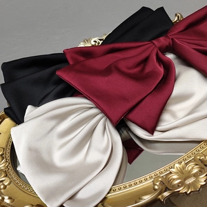 Elegant oversized satin bow hair clips in burgundy, black, and cream on a vintage tray