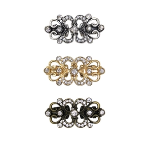 Three rhinestone sweater clips in silver, gold and bronze finishes on a white background