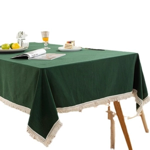 Modern green cotton table cloth with cream fringe tassels on a wooden dining table