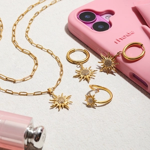 Flat lay of gold sun pendant necklace, matching hoop earrings and open ring set