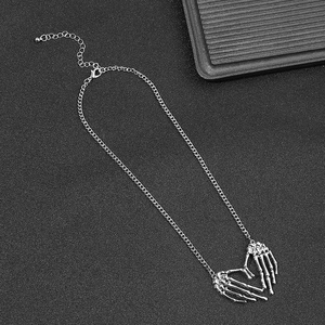 Gothic punk silver skeleton hand heart pendant necklace on textured black background