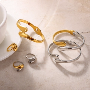 Polished minimalist gold and silver teardrop bangle and ring set on stone surface