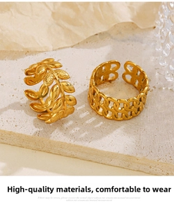 Detailed macro view of gold leaf band and hollow chain ring set on a textured surface