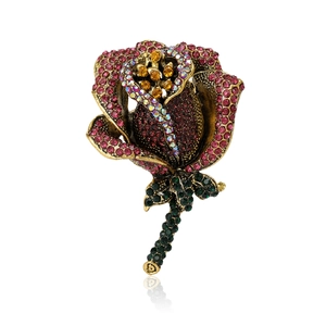 Elegant vintage rose brooch with red rhinestones and antique gold finish on white background
