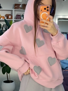 Détail d'un sweat à capuche rose oversize avec écussons cœurs et poignets côtelés