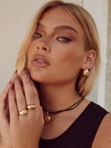 Détail de boucles d'oreilles goutte dorées et bague épaisse sur mannequin style rétro