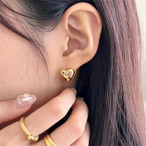 Close-up of heart-shaped gold earring with green and pink gemstones on a female model