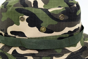 Detail of ripstop camouflage boonie hat fabric with golden metal air vents and webbing