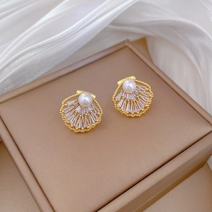 Detailed shot of gold shell earrings with centered pearl and sparkling zircon accents
