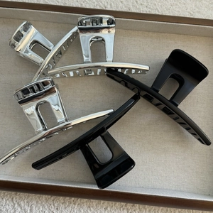 Minimalist silver and black hair claws in geometric cutout design on beige tray