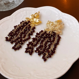 Detail of vintage grapevine leaf earrings with deep red bead tassels on white plate