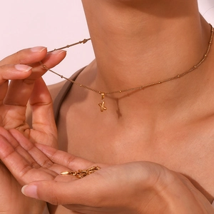 Close-up of a minimalist 18K gold plated stainless steel bubble X letter pendant on neck