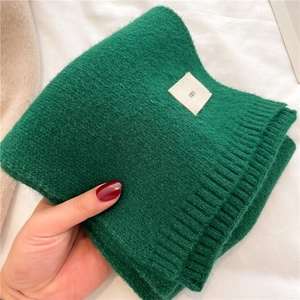 Close-up of green knitted scarf with emo logo label held by a hand on white fabric