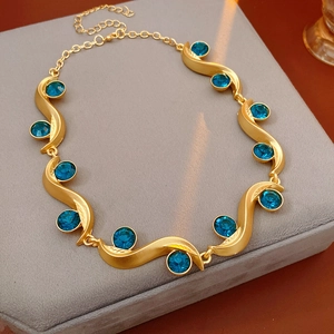 Macro detail of vintage gold wavy link necklace with embedded blue gemstones