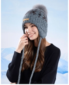 Detail of grey winter knit trapper hat with faux fur pompom and leather brand tag