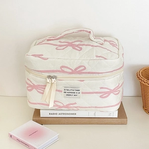 Quilted makeup bag with pink bow pattern and double zippers placed on books