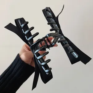 Detail view of large black double-layer fabric bow hair claw clip held by hand