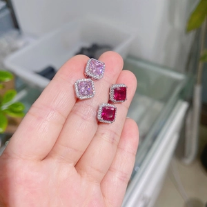Close-up of square cut red and pink ruby earrings held by hand in a halo setting