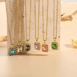 Detail of square zircon pendants on gold titanium chains over a beige stone background