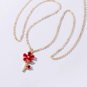 Detailed close-up of a gold chain necklace with a ruby red five-petal floral pendant