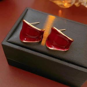Dettaglio orecchini a forma di C in smalto bordeaux con bordi dorati su scatola