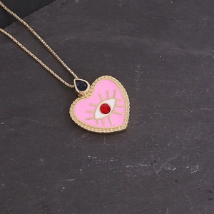 Close-up of a pink heart necklace with a red eye gem on a textured stone surface