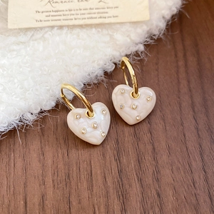 Detailed view of heart-shaped enamel earrings with sparkling rhinestones on wood surface