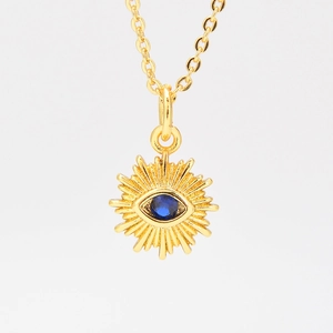 Golden necklace with sunburst evil eye pendant and blue zircon stone on white background