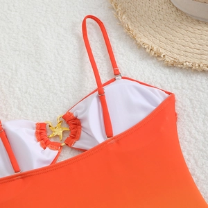 Dettaglio del top bikini arancione con fibbia a stella marina dorata su fondo soffice