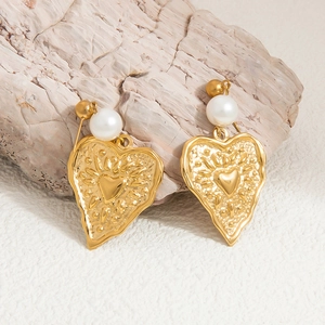 Macro detail of hammered gold heart earrings with pearl inlay on textured stone