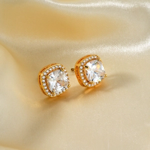 Macro shot of gold-plated square zircon stud earrings on elegant champagne silk fabric