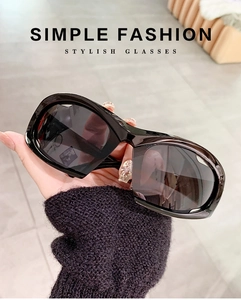 Detail of black chunky frame Y2K sports sunglasses with dark lenses held by hand