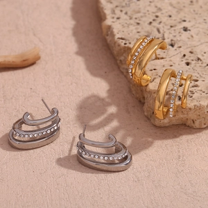 Detailed macro view of triple-layer C-shape gold and silver stud earrings with crystals