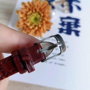 Detail of burgundy leather watch strap with polished silver buckle and tonal stitching