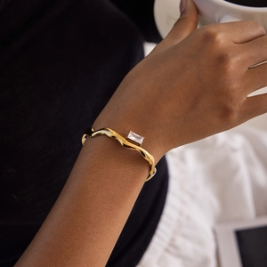 Close-up of a gold wavy cuff bracelet with a rectangle zircon on a model wrist