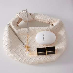 Flat lay of pearl pendant necklace on white woven leather bag with designer cosmetics